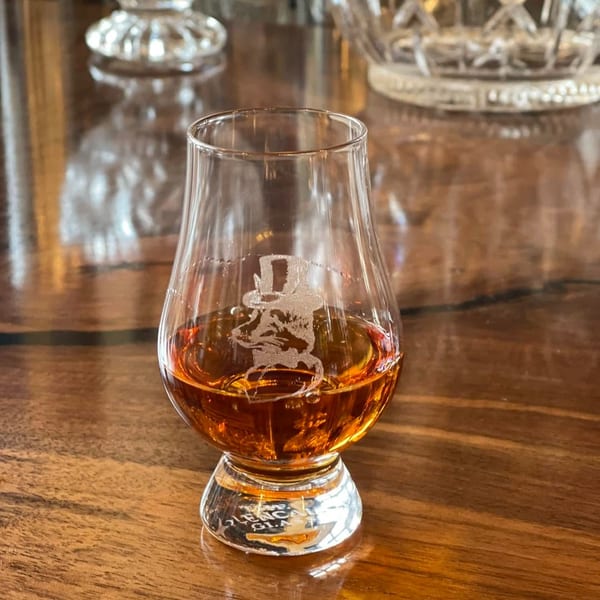 A Glencairn glass filled with amber whiskey, featuring an etched logo, on a wooden table.