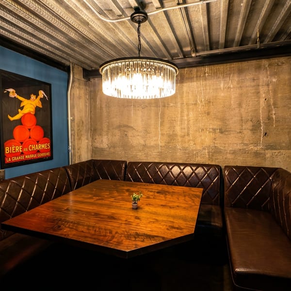 Cozy restaurant booth with brown leather seating, a wooden table, and vintage posters on blue and concrete walls.