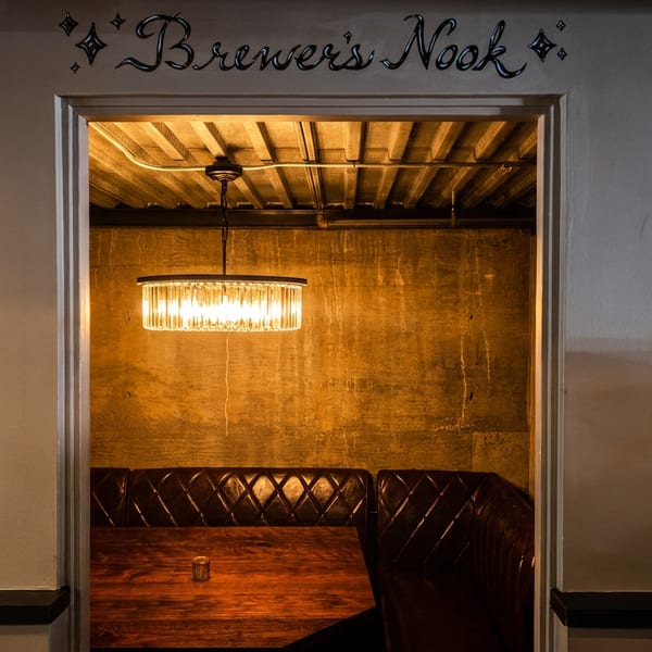 An inviting booth with dark leather seating and a wooden table, illuminated by a modern chandelier.