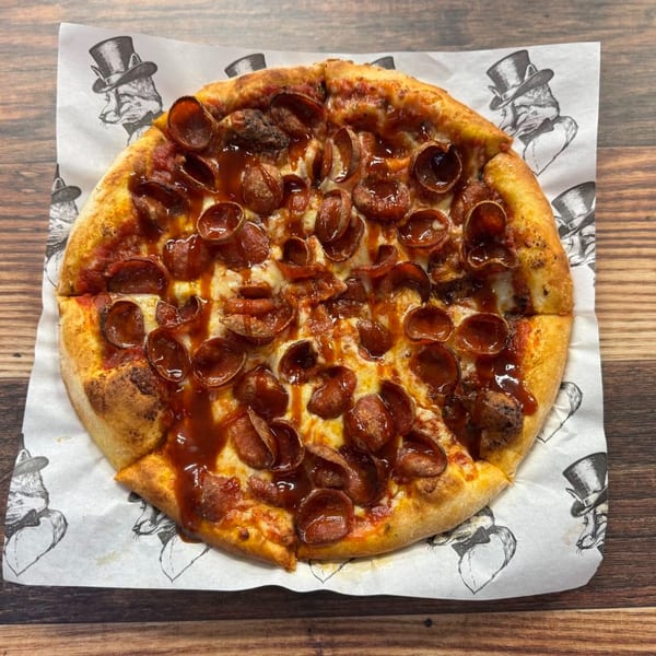 A pepperoni pizza with barbecue sauce drizzle on branded parchment paper, on a wooden table.