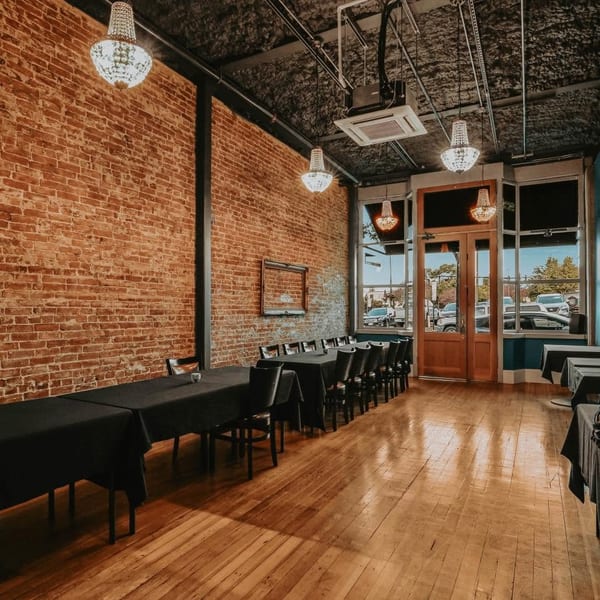 An empty event space with long tables, black tablecloths, brick walls, and chandeliers.