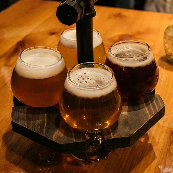 Four glasses of craft beer in a flight on a wooden table, with a decorative candle nearby.
