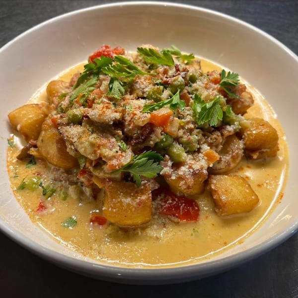 Golden-brown gnocchi in a creamy sauce with vegetables, parmesan, and fresh parsley in a white bowl.