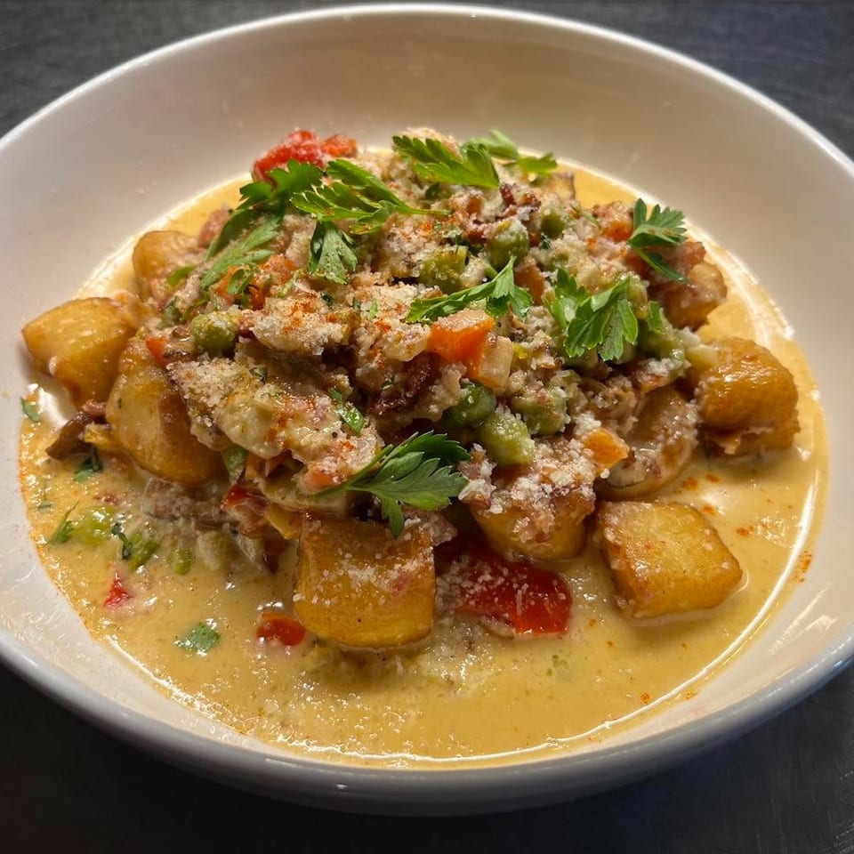 Golden-brown gnocchi in a creamy sauce with vegetables, parmesan, and fresh parsley in a white bowl.
