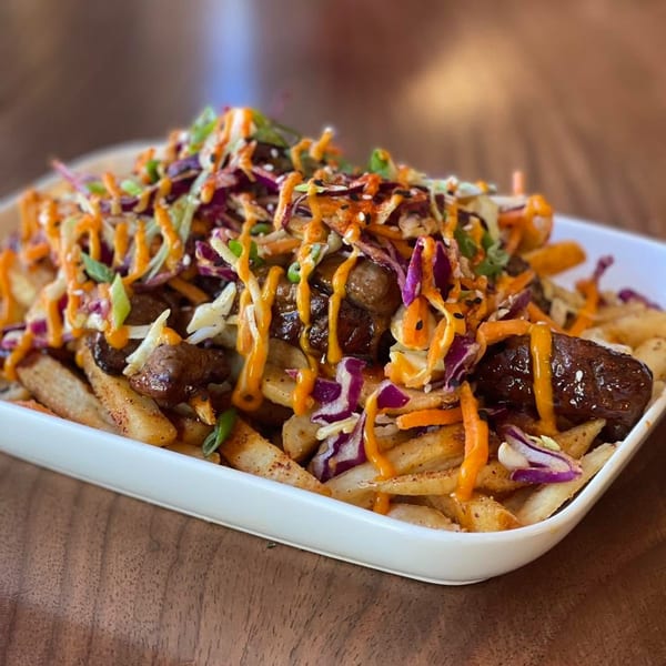 A white rectangular plate filled with french fries topped with meat, coleslaw, and orange sauce.
