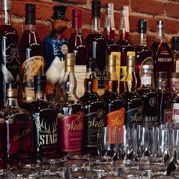 A collection of various bourbon and whiskey bottles, including Weller, Stagg, and Eagle Rare, with glasses.