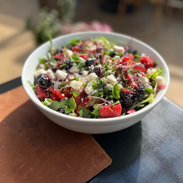 A vibrant berry and feta salad in a white bowl on a dark table with a brown menu.