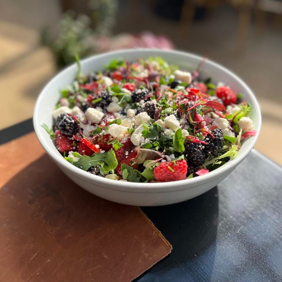 A vibrant berry and feta salad in a white bowl on a dark table with a brown menu.